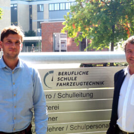 Herr Garbelmann und Herr Wranik vor dem Schullogo