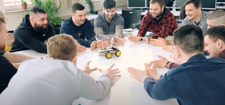 Schüler der Techniker Schule sitzen lachend am Tisch und betrachten ein kleines Elektroauto